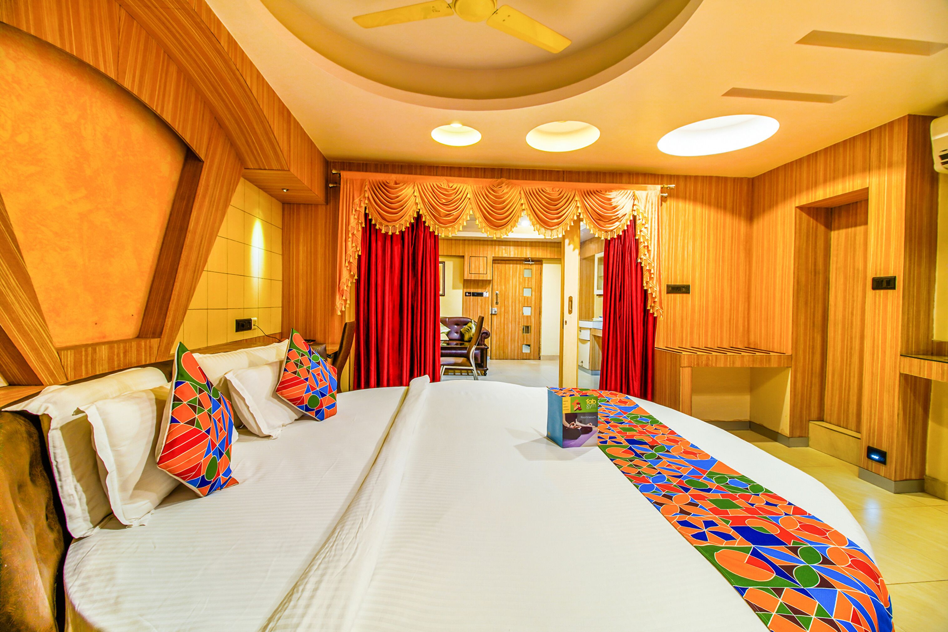 Une chambre d’hôtel avec un grand lit, deux tables de chevet, un ventilateur de plafond et une vue sur le couloir.