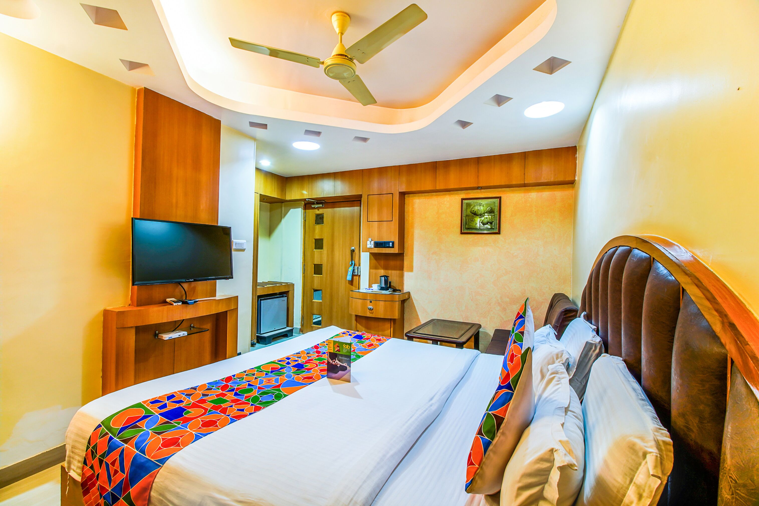 A hotel room with a bed, a television, a desk, and a ceiling fan.