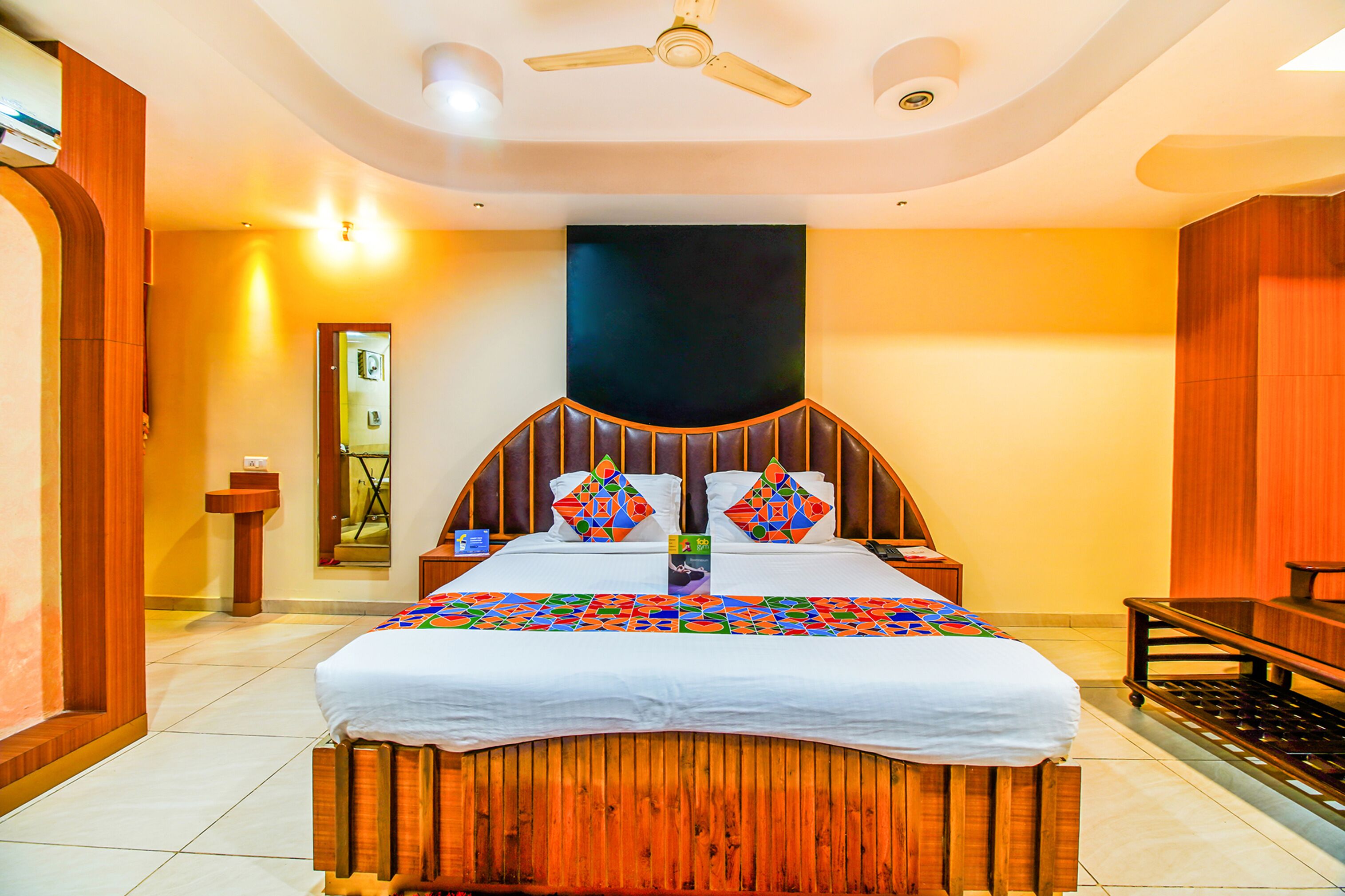 A hotel room with a large bed, wooden headboard, and a ceiling fan.