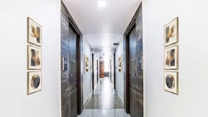 A hallway with framed artwork on the walls, a polished floor, and a door at the end. - FabHotel Crown Heights - Nr. Kormangala Club (Bengaluru)