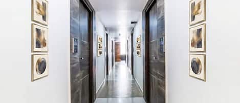A hallway with framed artwork on the walls, a polished floor, and a door at the end.