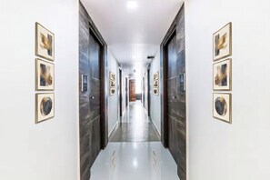 A hallway with framed artwork on the walls, a polished floor, and a door at the end. - FabHotel Crown Heights - Nr. Kormangala Club (Bengaluru)