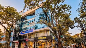 A multi-story building with a glass facade, a sign for 'Ree Agie' on the upper level, and a 'Chaska Bun' bakery on the ground floor. - FabHotel Crown Heights - Nr. Kormangala Club (Bengaluru)