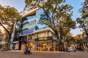A multi-story building with a glass facade, a sign for 'Ree Agie' on the upper level, and a 'Chaska Bun' bakery on the ground floor. - FabHotel Crown Heights - Nr. Kormangala Club (Bengaluru)