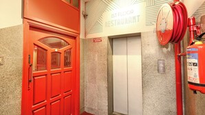 A red double door with a glass panel, a sign indicating the 1st floor restaurant, a non-smoking zone sign, and a fire extinguisher mounted on the wall. - FabHotel Santhi Inn (Puducherry)