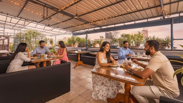 A rooftop restaurant with outdoor seating, potted plants, and a view of the city skyline. - FabHotel Santhi Inn (Puducherry)