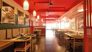 A restaurant interior with wooden tables and chairs, hanging pendant lights, and framed pictures on the walls. - FabHotel Santhi Inn (Puducherry)