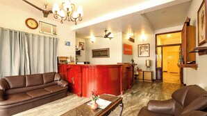 A spacious living area with a red reception desk, leather sofas, a wooden coffee table, and a chandelier. - FabHotel Santhi Inn (Puducherry)