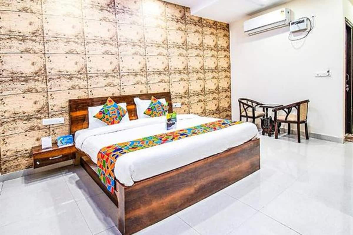 Une chambre d’hôtel avec un lit en bois, une petite table de chevet, une chaise et un climatiseur fixé au mur.