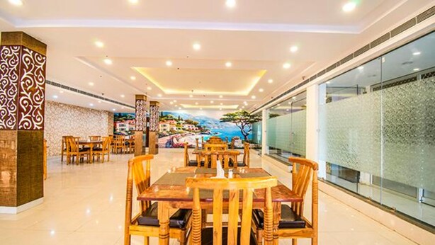 A spacious restaurant with wooden tables and chairs, a mural of a coastal scene, and a modern ceiling design. - Fabhotel Elysian Grand (Lucknow)