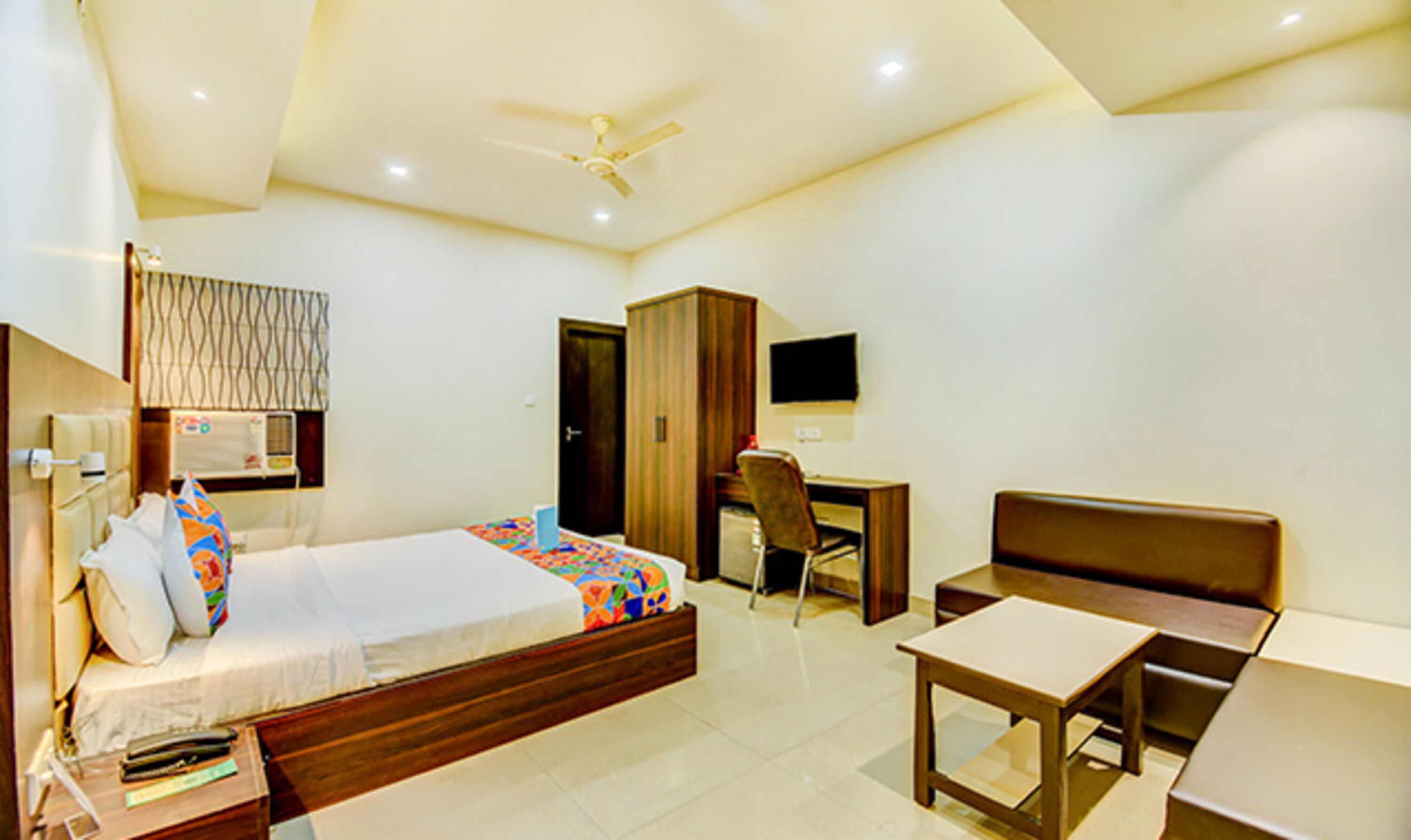 A hotel room with a bed, desk, chair, and a television on the wall.