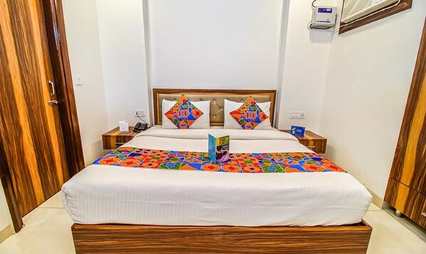 Una cama bien tendida con un colcha de colores, un cabecero de madera y una mesita de noche con una lámpara y un teléfono.