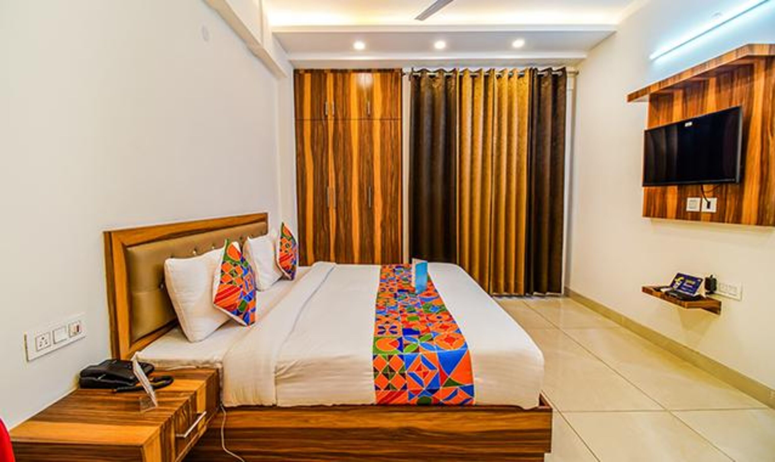Una habitación de hotel con una cama de madera, un televisor montado en la pared y un estante pequeño con un control remoto.