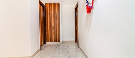 Un pasillo con una puerta de madera, un extintor en la pared y suelo de baldosas.