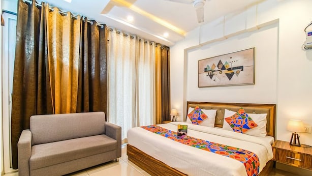 A hotel room with a bed, a sofa, a ceiling fan, a nightstand, and a painting on the wall. - Fabhotel Kiara (Gurugram)