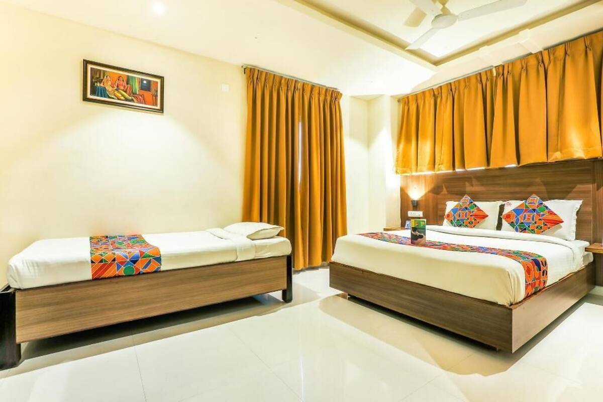 A hotel room with two beds, a ceiling fan, a painting on the wall, and a window with curtains.