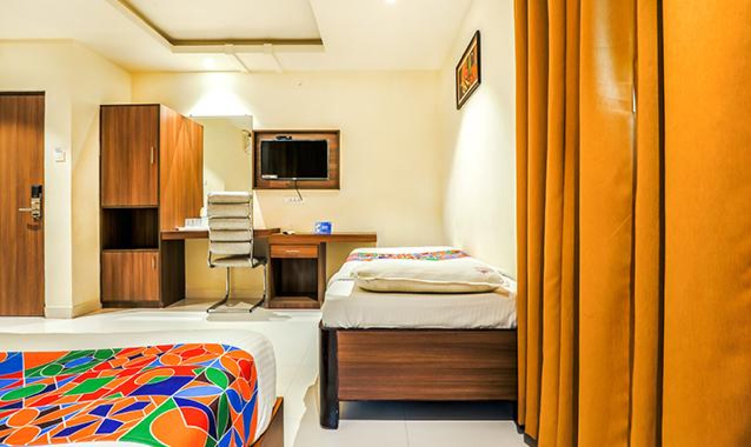 A hotel room with two beds, a desk, a chair, a television, and a wardrobe.