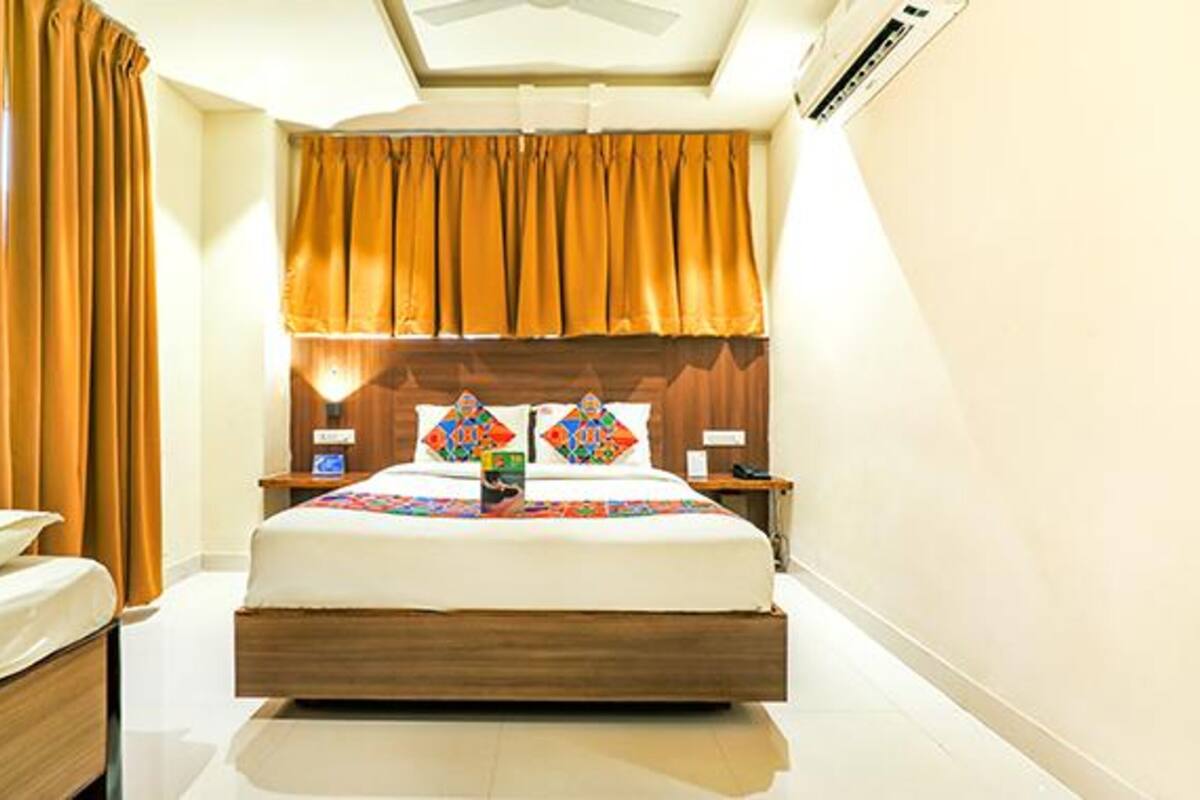 A hotel room with a wooden bed, two bedside tables, a nightstand, a wall-mounted air conditioner, and a ceiling fan.