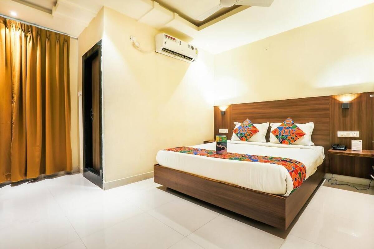 A hotel room with a bed, an air conditioning unit, a nightstand, and a wooden headboard.