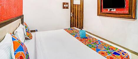 A hotel room with a bed, pillows, a small table, a TV, and a door.