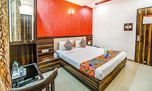 Una habitación de hotel con cama, escritorio con silla, armario de madera y pared texturizada de color rojo.
