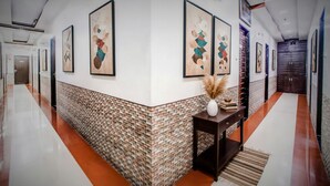 A hallway with a patterned wall, framed artwork, a small table with a vase, and a door at the end. - Fabhotel The Adore Palace (Mumbai)