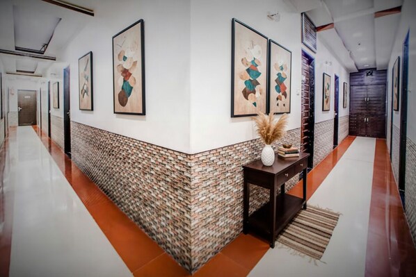 Um corredor com parede estampada, obras de arte emolduradas, uma pequena mesa com um vaso e uma porta no final.