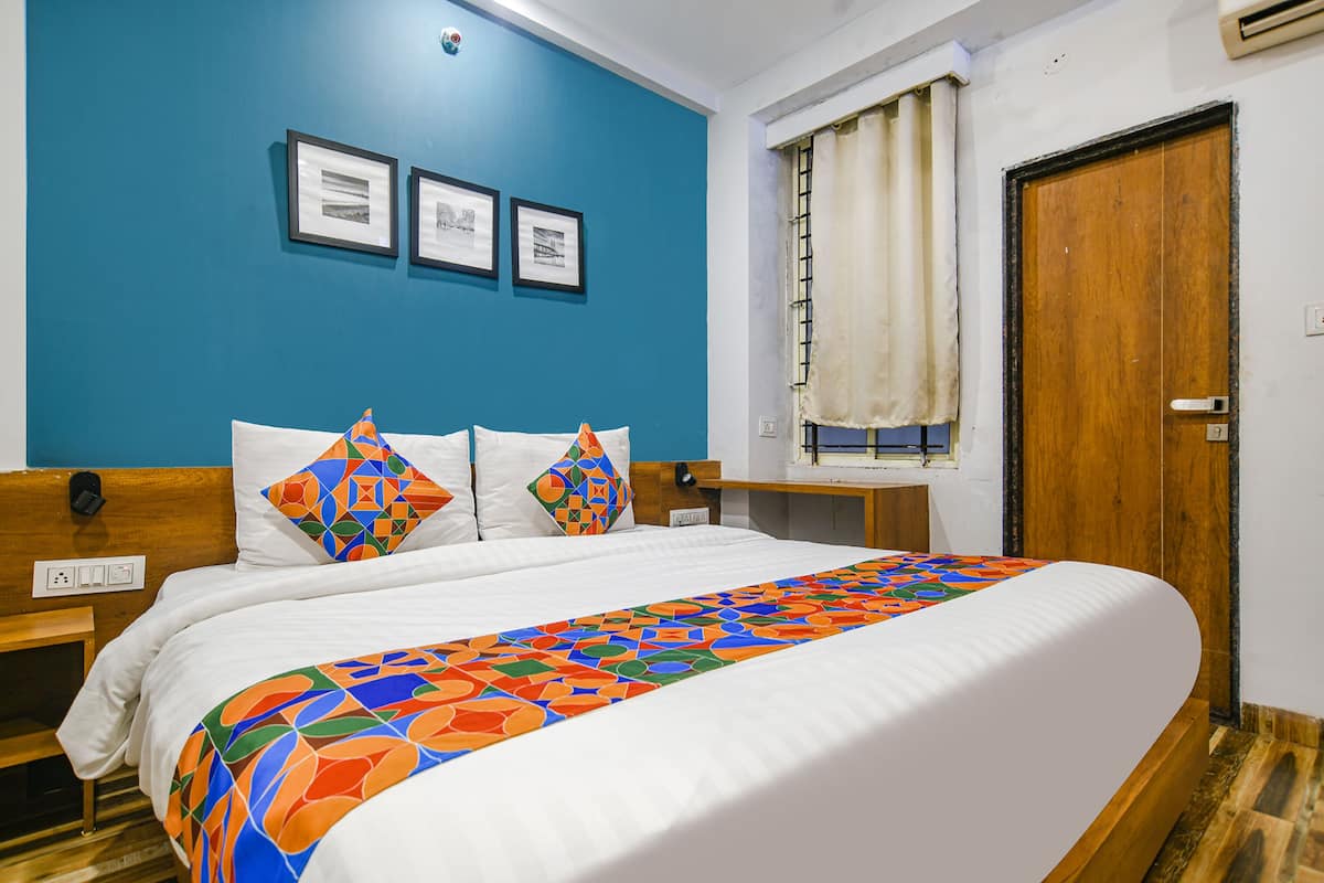 A neatly made bed with a colorful geometric-patterned bedspread, a wooden headboard, and a wall with three framed pictures.