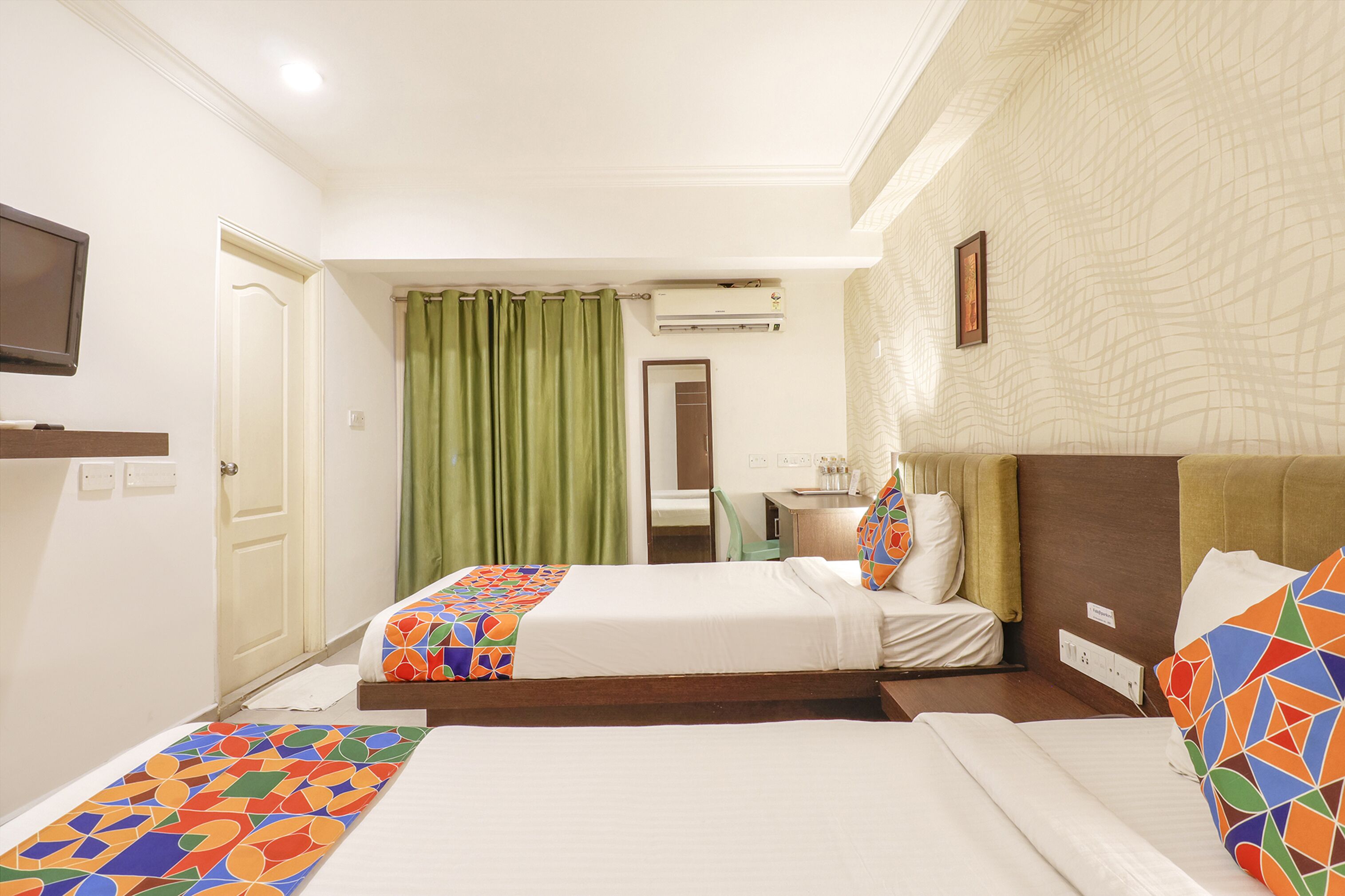 A hotel room with two beds, a television, an air conditioning unit, and a green curtain.