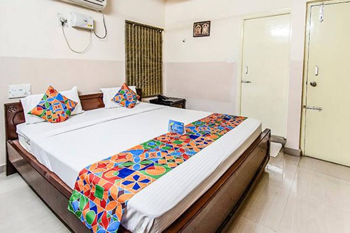 Uma cama bem arrumada com um cobertor colorido, uma mesa de cabeceira, um ar condicionado fixado na parede e uma porta.