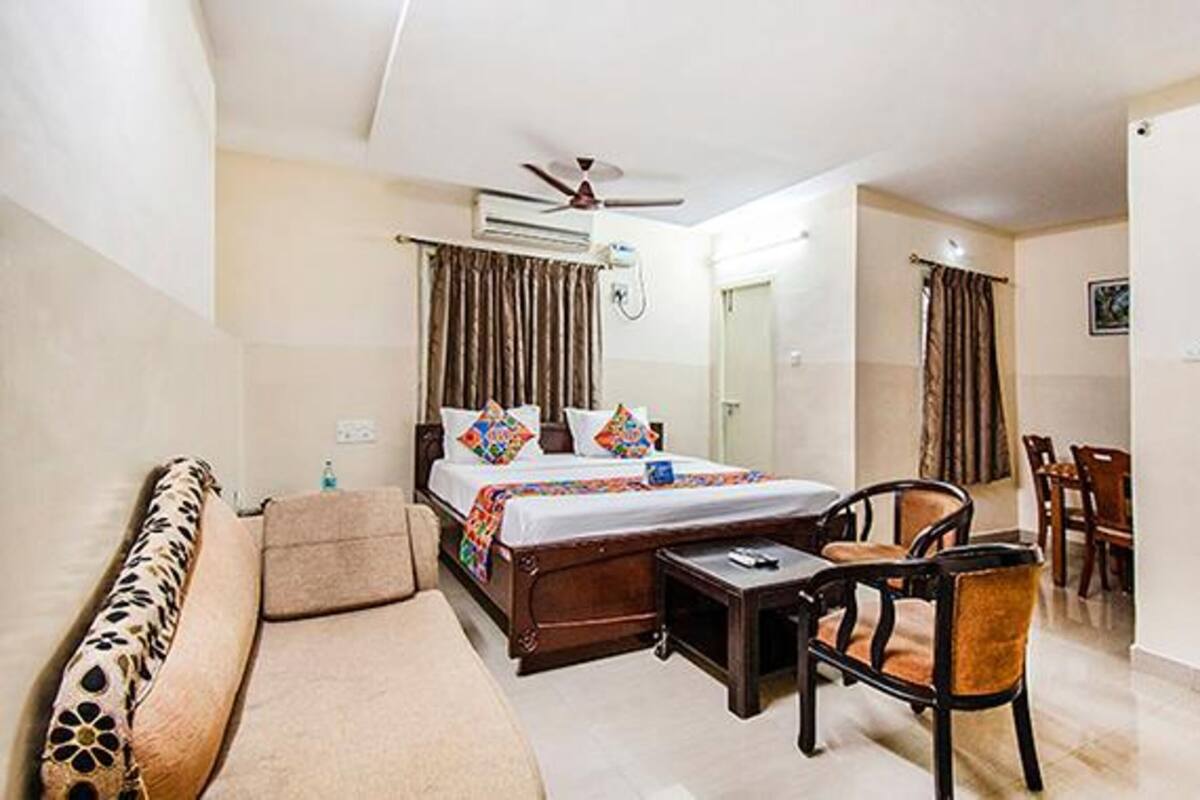 Quarto de hotel com cama, sofá, poltrona, mesa pequena e ventilador de teto.