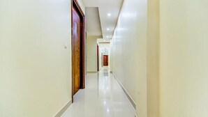 A long, narrow hallway with a wooden door on the left and a red door at the end. The floor is tiled, and the walls are plain. - FabHotel Nayyar Inn (Amritsar)