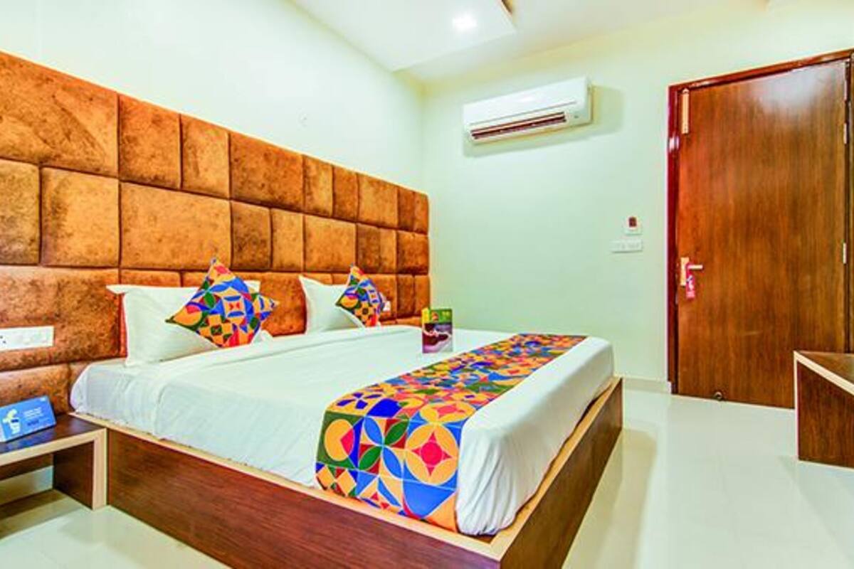 A hotel room with a wooden headboard, a bed with colorful bedding, a bedside table with a lamp, and a wooden door.