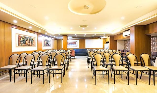 Un salón de conferencias con filas de sillas, un escenario y obras de arte enmarcadas en las paredes.
