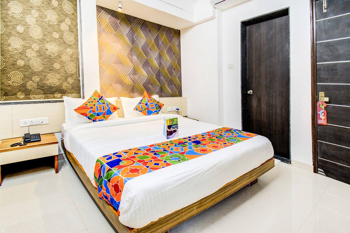 A hotel room with a large bed, a bedside table with a phone, and a wall with patterned wallpaper.