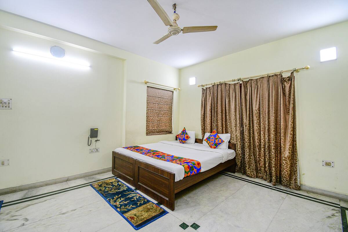 A bedroom with a bed, curtains, a ceiling fan, a wall-mounted phone, and a patterned rug.