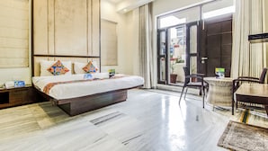 Habitación de hotel con una cama grande, una mesita pequeña y una silla. Posee un ventanal corredero que da a un espacio exterior.