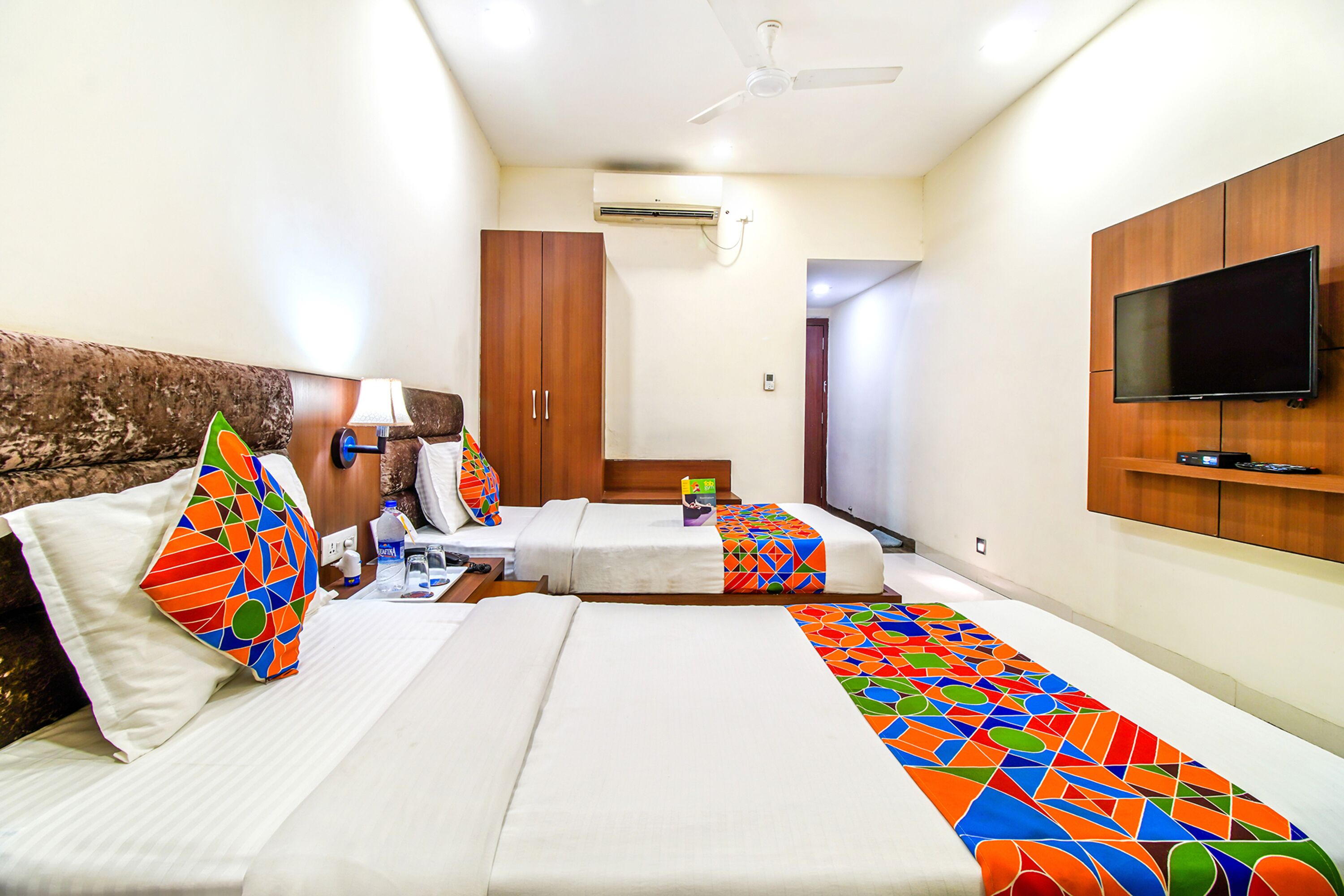 A hotel room with two beds, a TV, an air conditioner, and a ceiling fan.