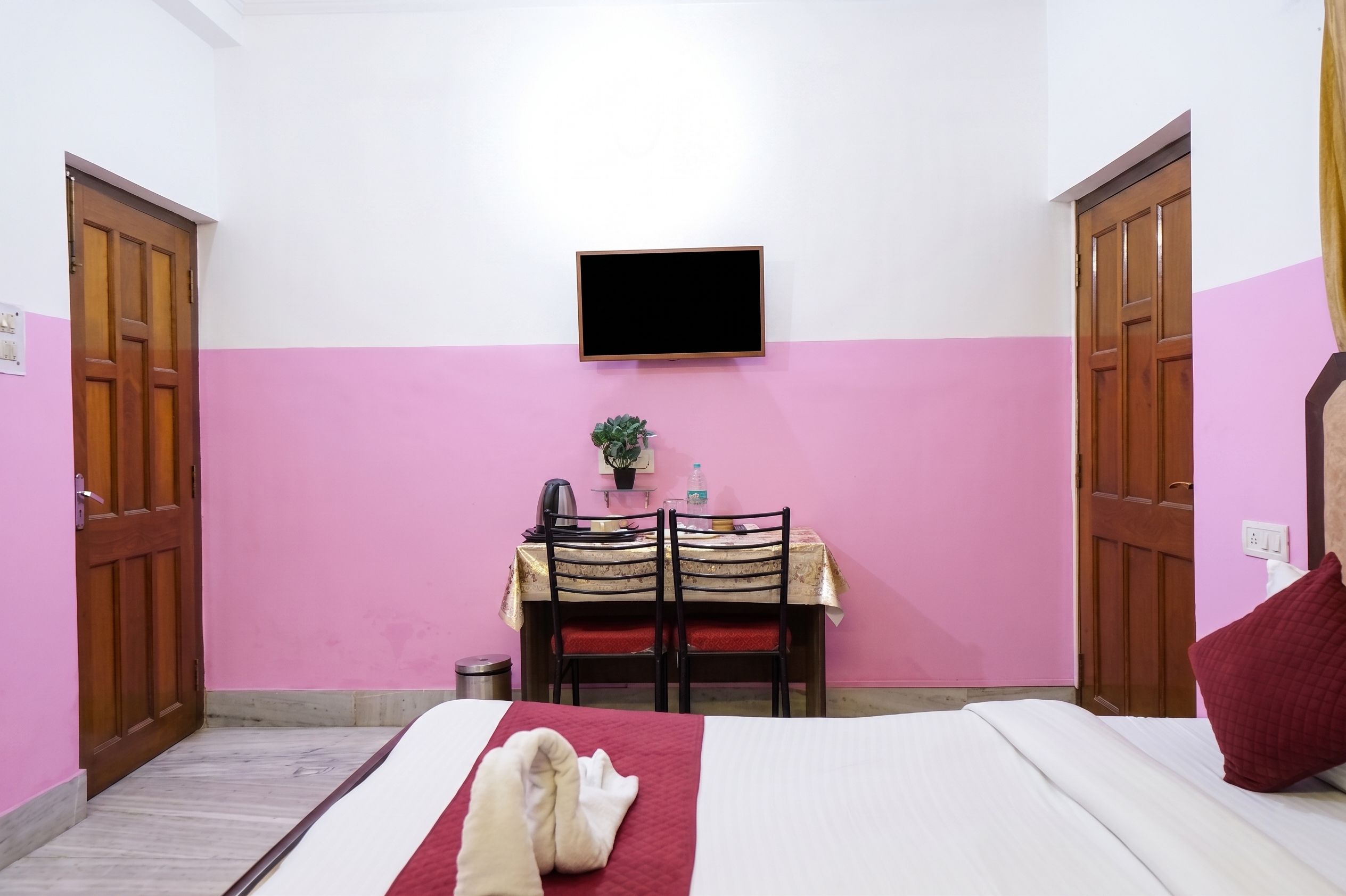 A room with a bed, a desk with a chair, a television mounted on the wall, and a small potted plant.