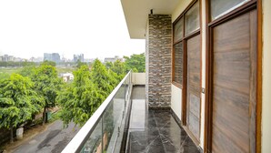 A balcony with a glass railing overlooking a cityscape and greenery. - FabHotel A&V Hospitality (Noida)
