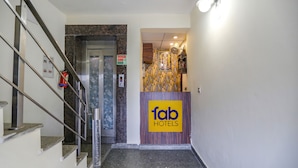 A hotel reception area with a marble staircase, a reception desk, and a wall-mounted light fixture. - FabHotel A&V Hospitality (Noida)