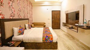 A hotel room with a bed, a sofa, a TV, and a small table with a kettle. - FabHotel A&V Hospitality (Noida)