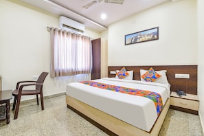 A hotel room with a bed, a desk, a chair, an air conditioner, and a painting on the wall. - Fabhotel Vardan Villa (Udaipur)