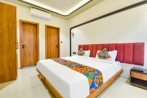 A modern hotel room with a large bed, wooden doors, a red upholstered headboard, and a small bedside table. - Vaibhavya Hotel and Restaurant-Udaipur (Udaipur)
