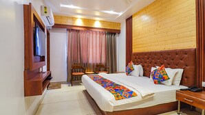 Una habitación de hotel con una cama grande, cabecera de madera, televisor montado en la pared y una ventana con cortinas.