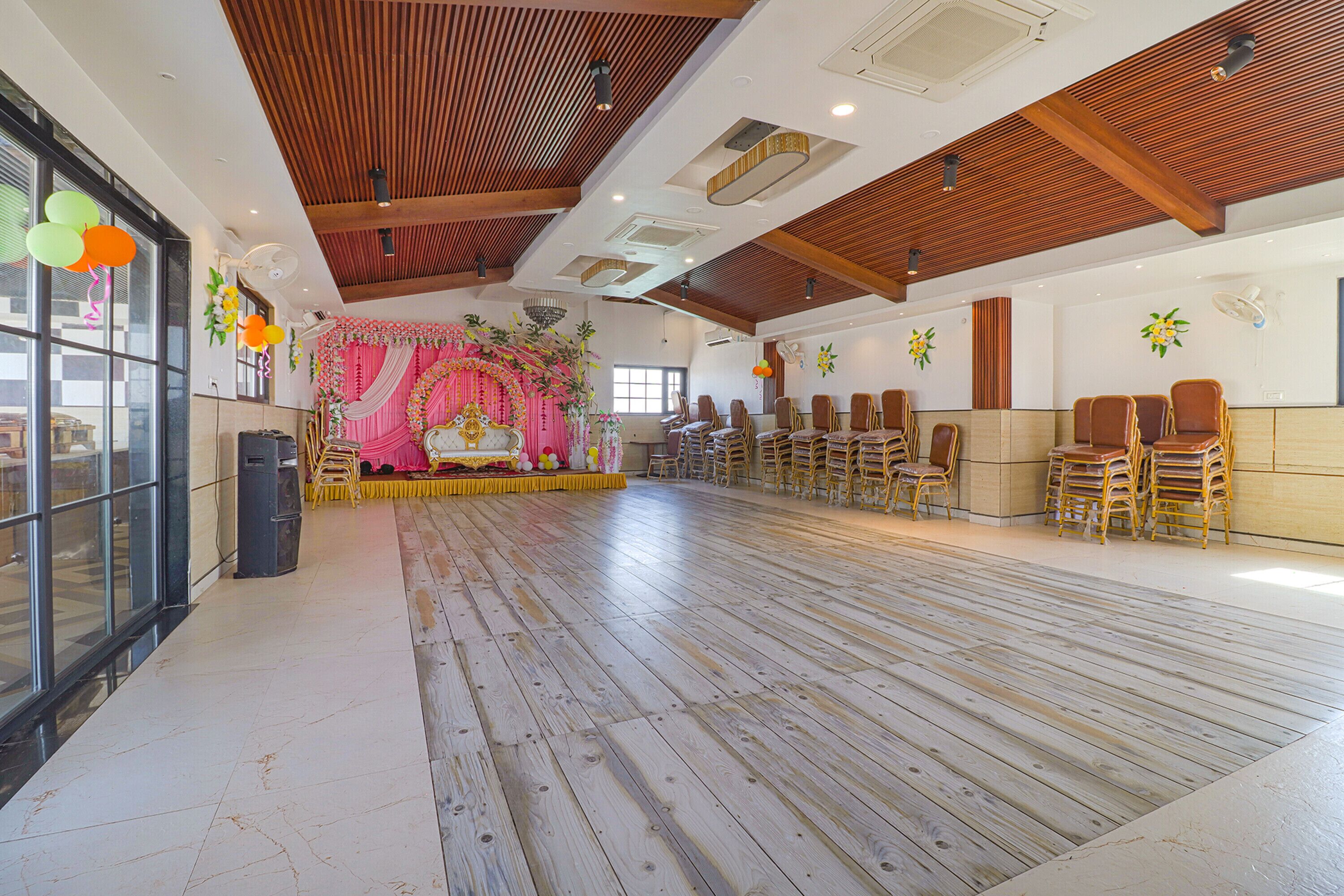 A spacious hall with a wooden floor, rows of chairs, and a stage with floral decorations.