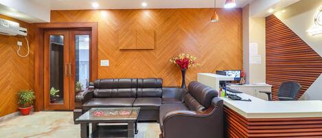 A reception area with a wooden herringbone wall, a brown leather sofa, a reception desk, and a potted plant.