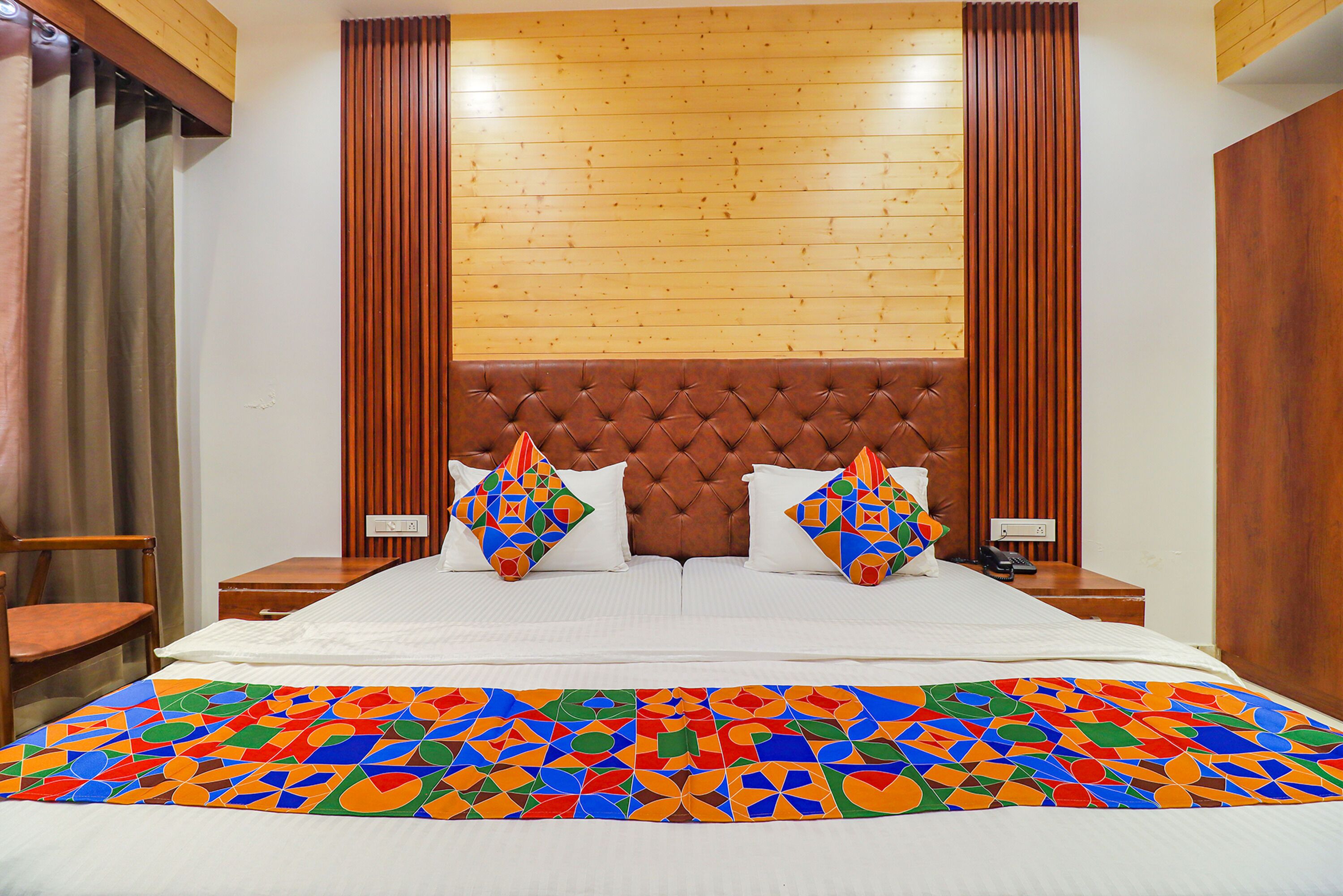 A hotel room with a large bed, wooden headboard, two nightstands, and a colorful geometric-patterned bedspread.