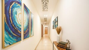 A hallway with abstract paintings on the walls, a wooden console table with books and a vase, and a decorative ceiling piece. - Fabescape Panchkula Motels (Dera Bassi)
