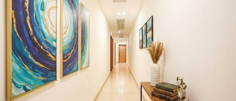 A hallway with abstract paintings on the walls, a wooden console table with books and a vase, and a decorative ceiling piece.
